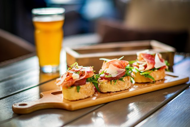Tabla de montaditos con jamón acompañados de una caña de cerveza