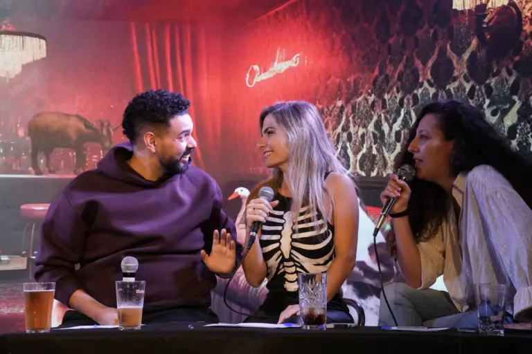 Tres artistas riéndose juntos a una mesa en el escenario