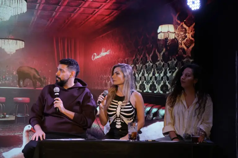 Tres invitados sentados a una mesa en el escenario con micrófonos