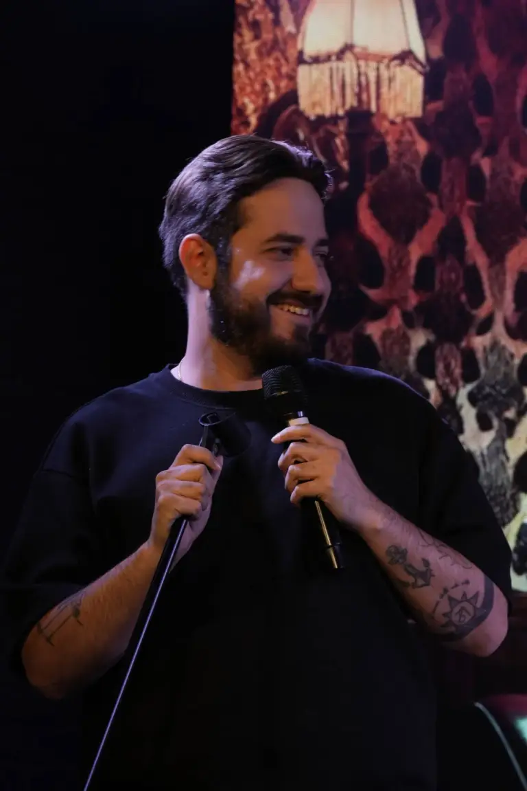 Cómico con camiseta negra sonriendo al micrófono