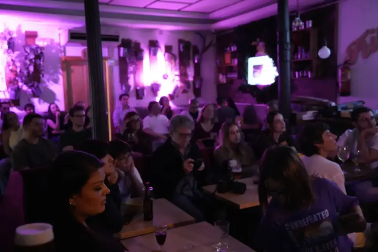 Público apiñado alrededor de las mesas bajo una luz morada