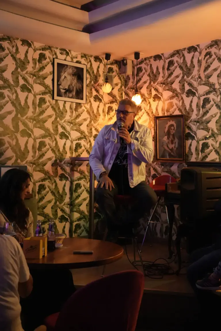 Cómico sentado en un taburete contando una historia junto a un cuadro enmarcado