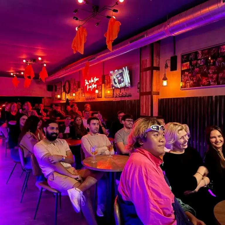 Público en sus mesas bajo luces rojas y moradas, esperando el espectáculo