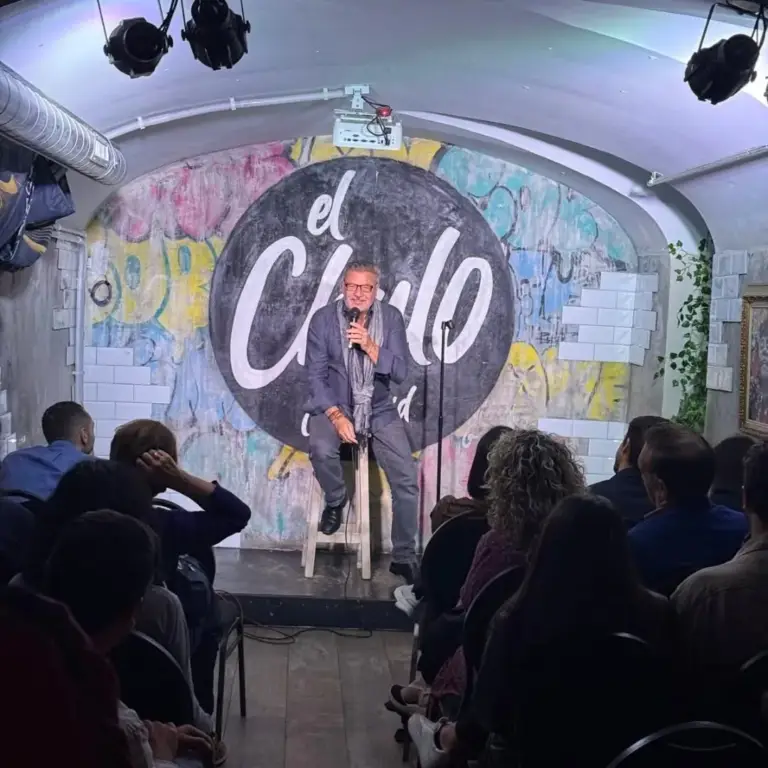 Cómico sentado en un taburete en el escenario de El Chulo, con la sala llena