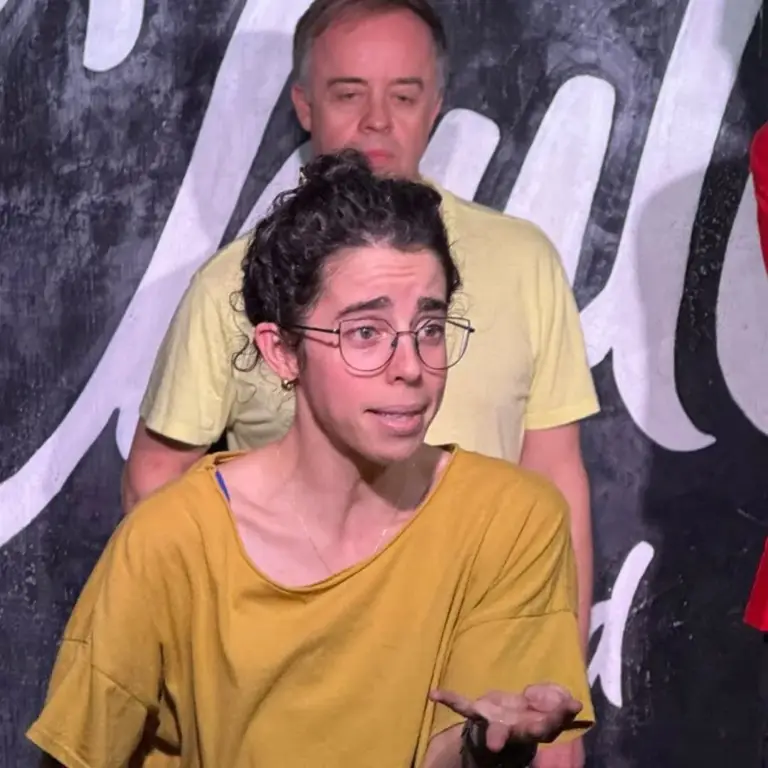 Actriz con gafas en plena escena, con un compañero de pie detrás
