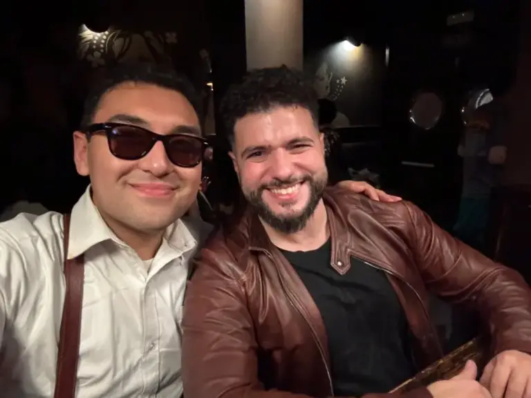 Dos artistas sonriendo para un selfi, uno con gafas de sol