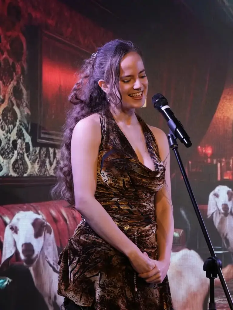 Cómica con vestido de estampado de leopardo sonriendo al micrófono delante de un fondo rojo