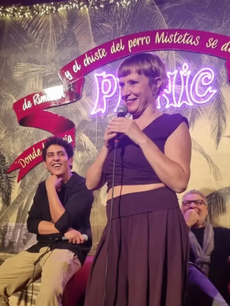 Cómica con top morado actuando en Picnic mientras dos artistas se ríen detrás