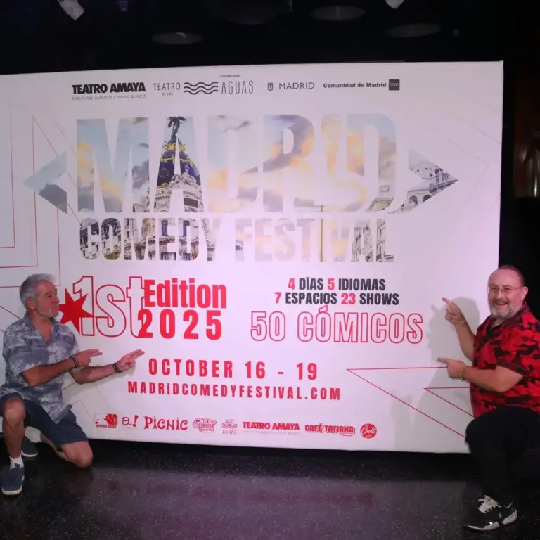 Dos hombres señalando el cartel de la primera edición de Madrid Comedy Festival en el escenario del Teatro Amaya