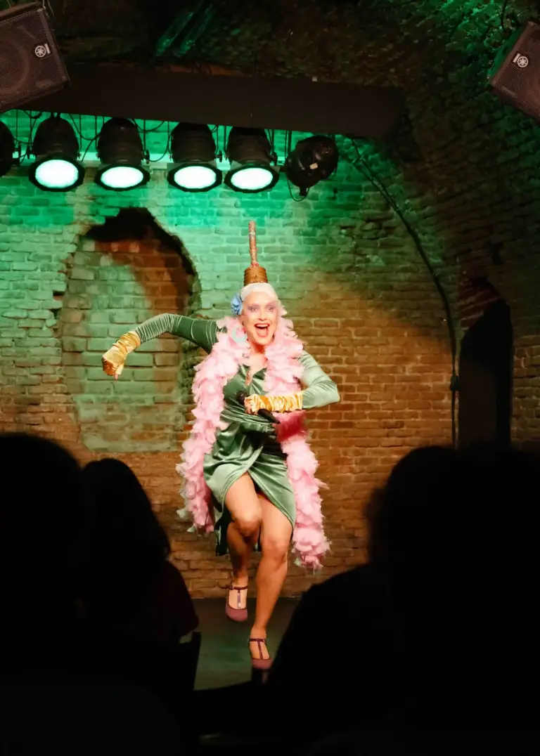 Artista con vestido verde y boa de plumas rosa levantando una pierna en el escenario