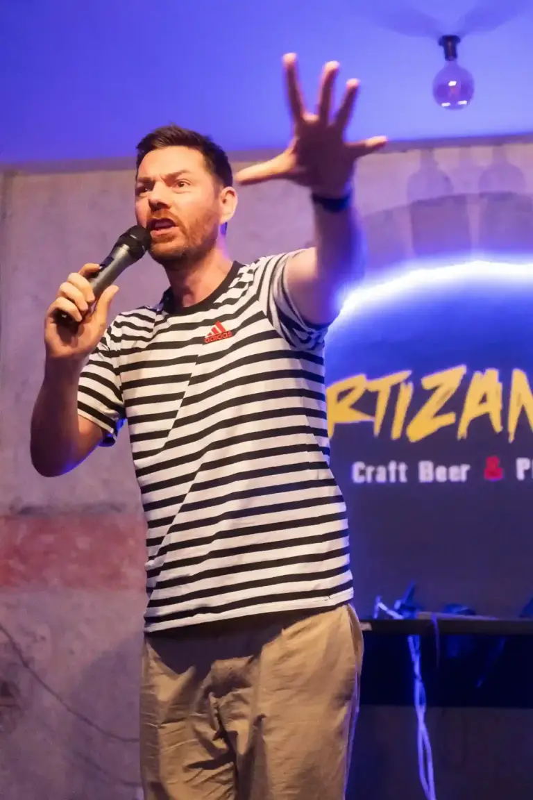 Cómico con camiseta de rayas inclinándose hacia el público en Artizanale
