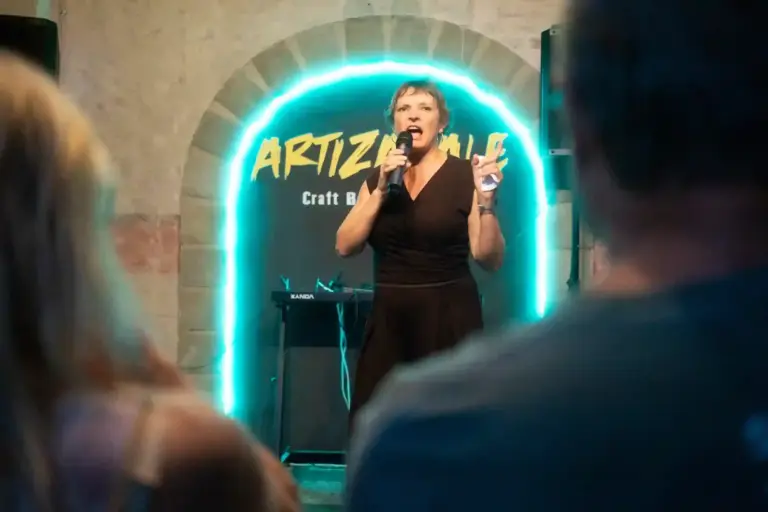 Cómica con vestido negro actuando bajo el arco de neón de Artizanale