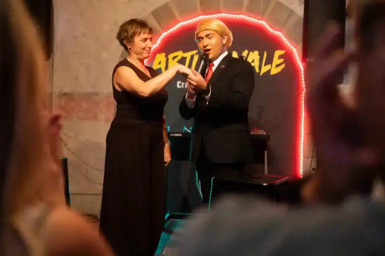 Dos artistas en el escenario de Artizanale, uno con peluca rubia y traje