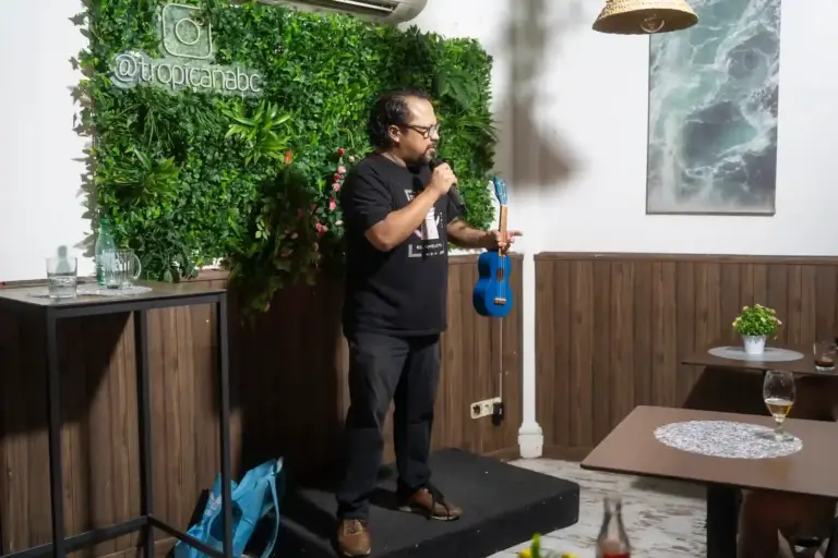 Cómico con un ukelele azul y un micrófono en Tropicana
