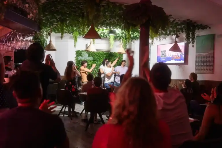 Público animando con los brazos en alto bajo luces rojas en Tropicana