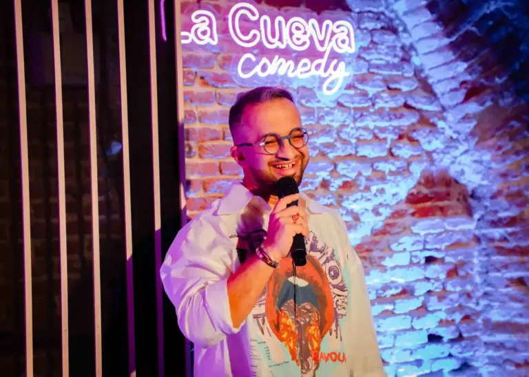 Cómico con gafas sujetando el micrófono junto a la pared de ladrillo de La Cueva Comedy