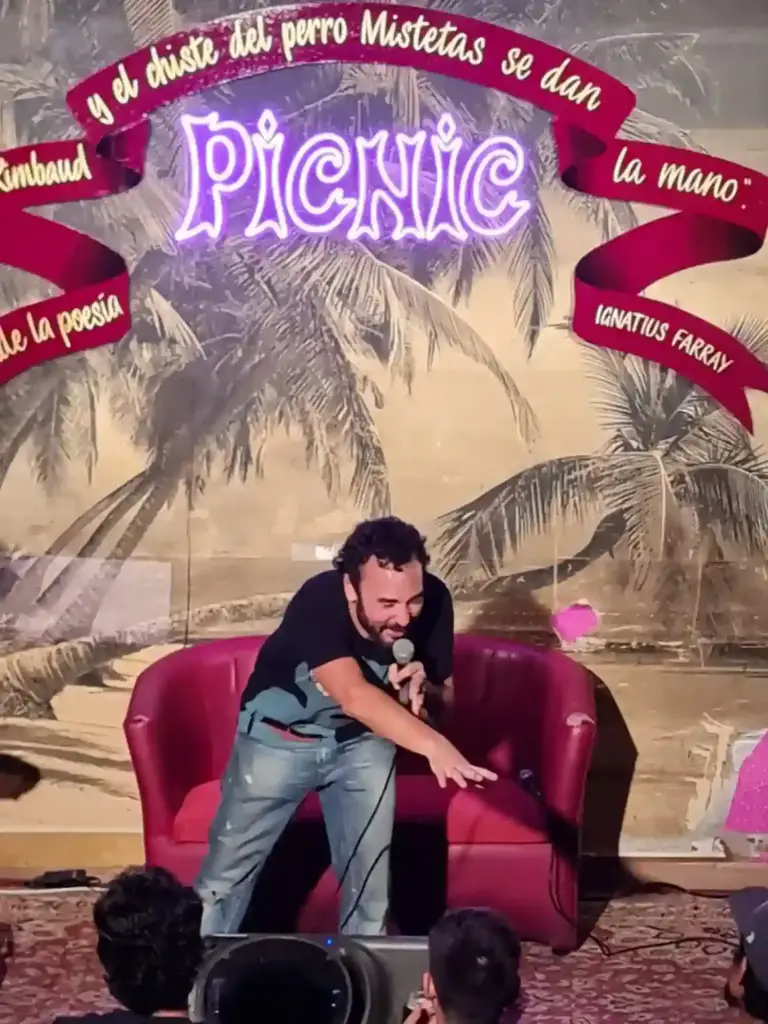 Cómico inclinándose hacia el público delante del sillón rojo del escenario de Picnic