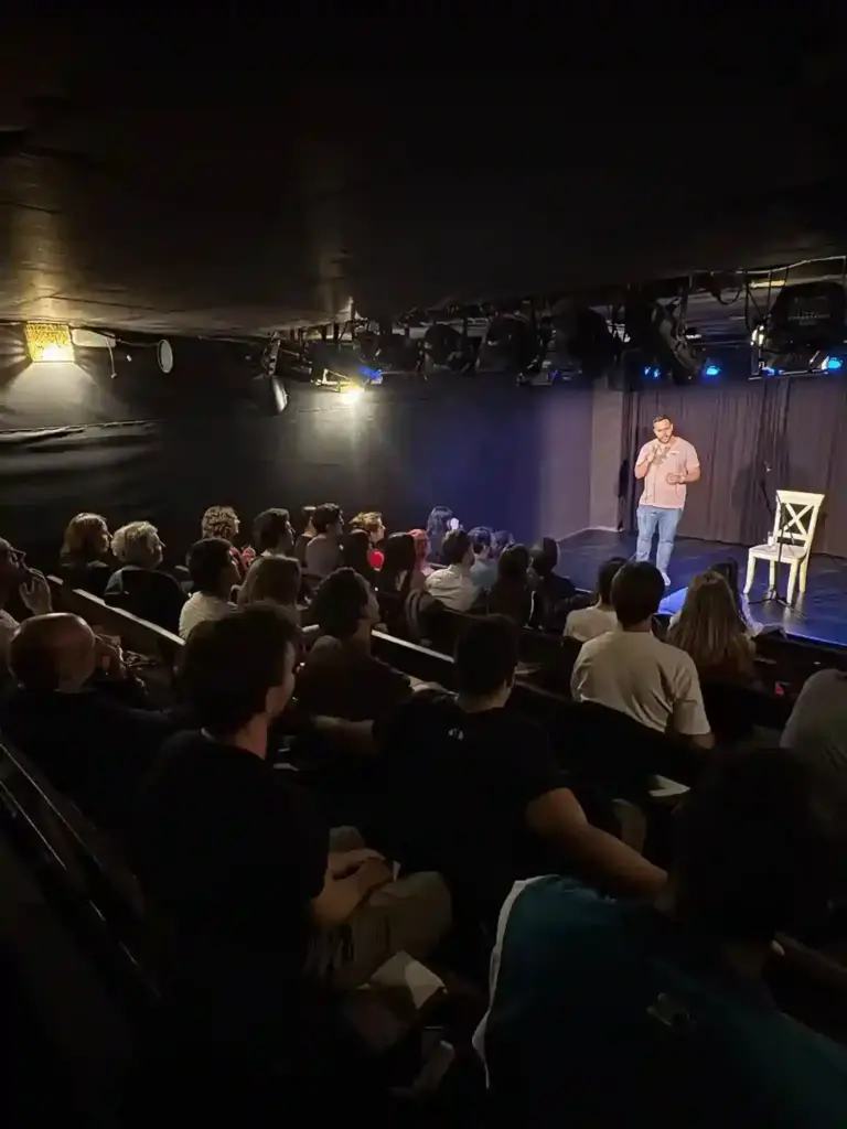Público en las gradas de un teatro viendo a un cómico en un escenario pequeño