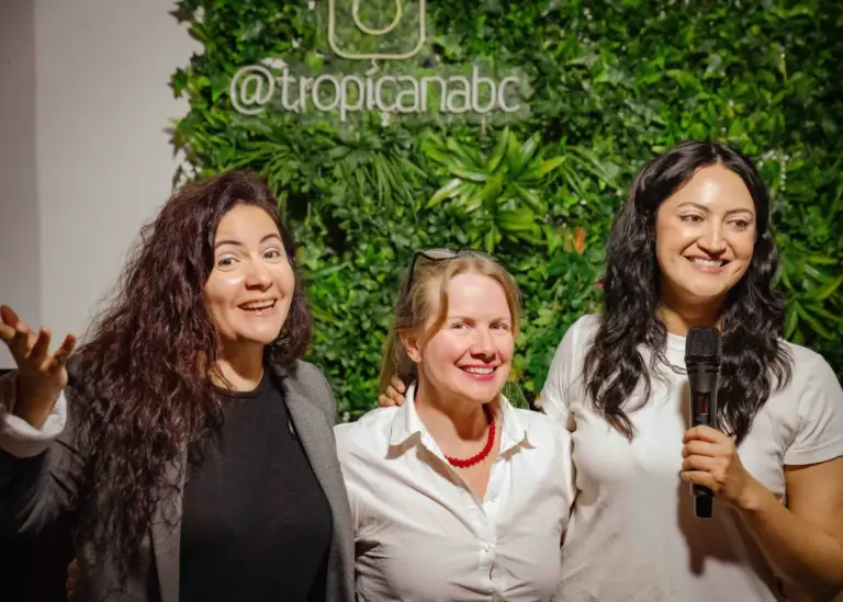 Tres cómicas sonriendo juntas delante de la pared de plantas de Tropicana